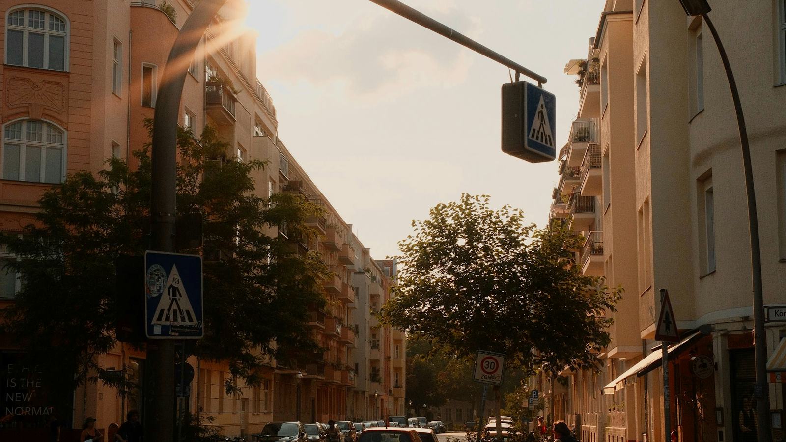A Berlin street lined with apartment buildings at golden hour, with a cyclist passing by