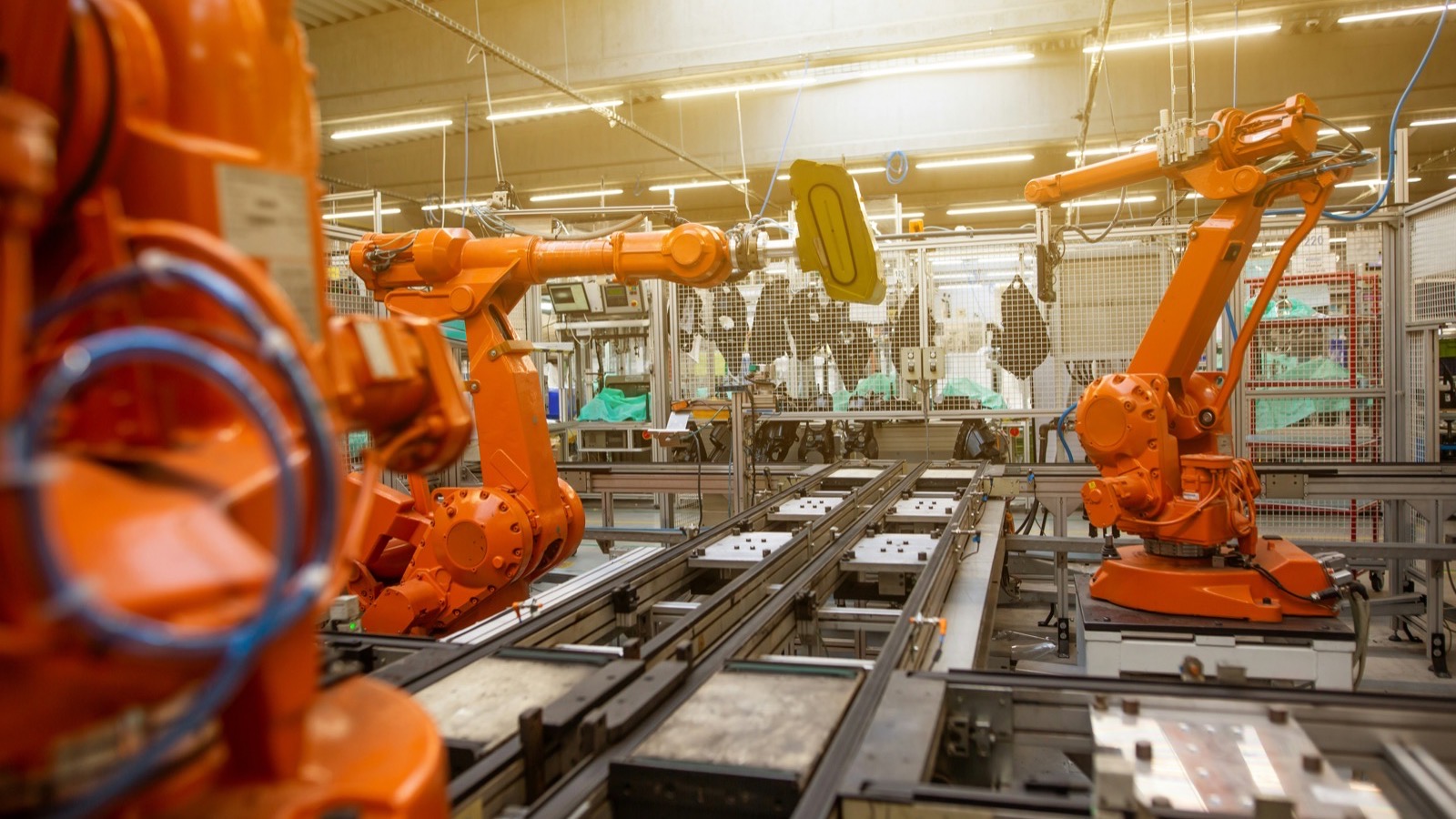 Orange industrial robot arms beside an automated production line in a factory hall.