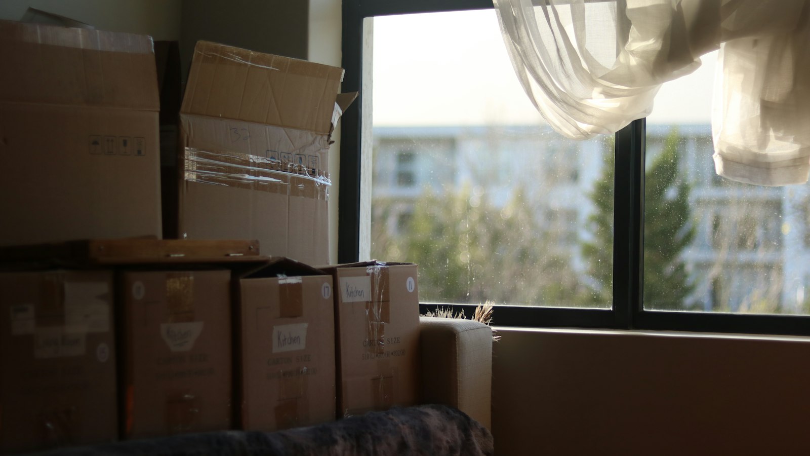 Moving boxes stacked in an empty room with a large window