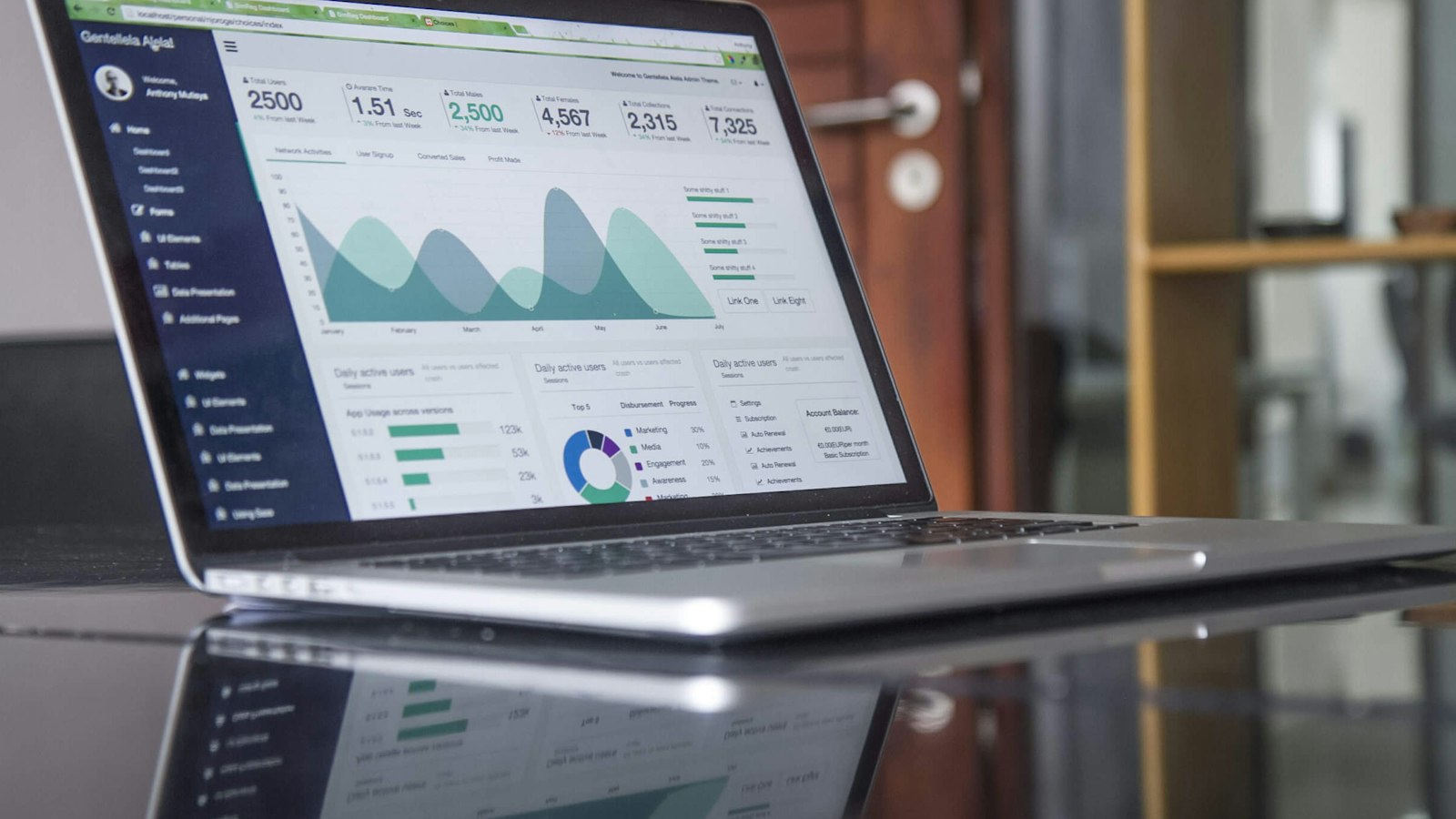 A laptop on a glass table showing a bar chart of statistics